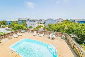 A residential area with a swimming pool, wooden deck, and lounge chairs. - Milo's Waves - Corolla, Ocean Sands, 50 Yards to Beach, Pool, Hot Tub, Pets OK (Corolla)