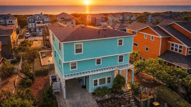 Ein zweistöckiges Haus mit Veranda und Blick auf den Ozean bei Sonnenuntergang.