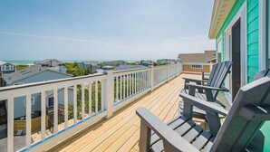 Eine Holzterrasse mit weißer Reling, die auf einen Strand und andere Gebäude blickt.