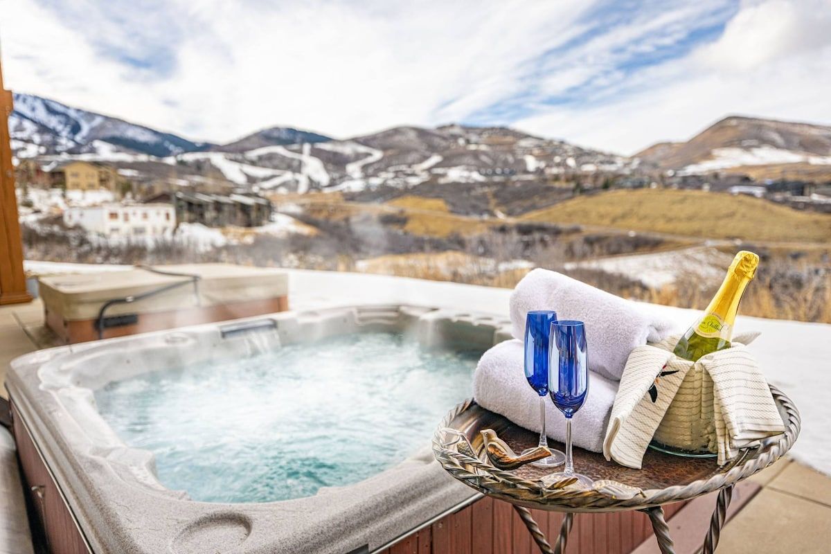 Un jacuzzi con vistas a la montaña, una botella de champán y dos copas sobre una mesa.
