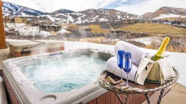 Un jacuzzi con vista a la montaña, una botella de champán y una toalla sobre una mesa.