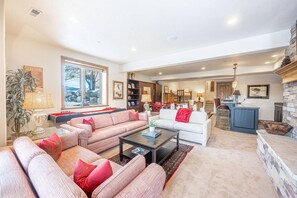A spacious living room with a large sofa set, a coffee table, and a fireplace. There is a kitchen area visible in the background.