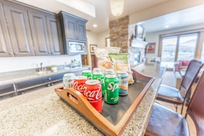 A kitchen counter with a tray holding soda cans and a bag of crisps.