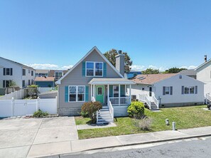 Une maison de plain-pied avec un porche à l’avant, un petit jardin devant et un ciel bleu dégagé.