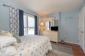 Une chambre à coucher avec un lit, une commode, une télévision et une fenêtre avec des rideaux.