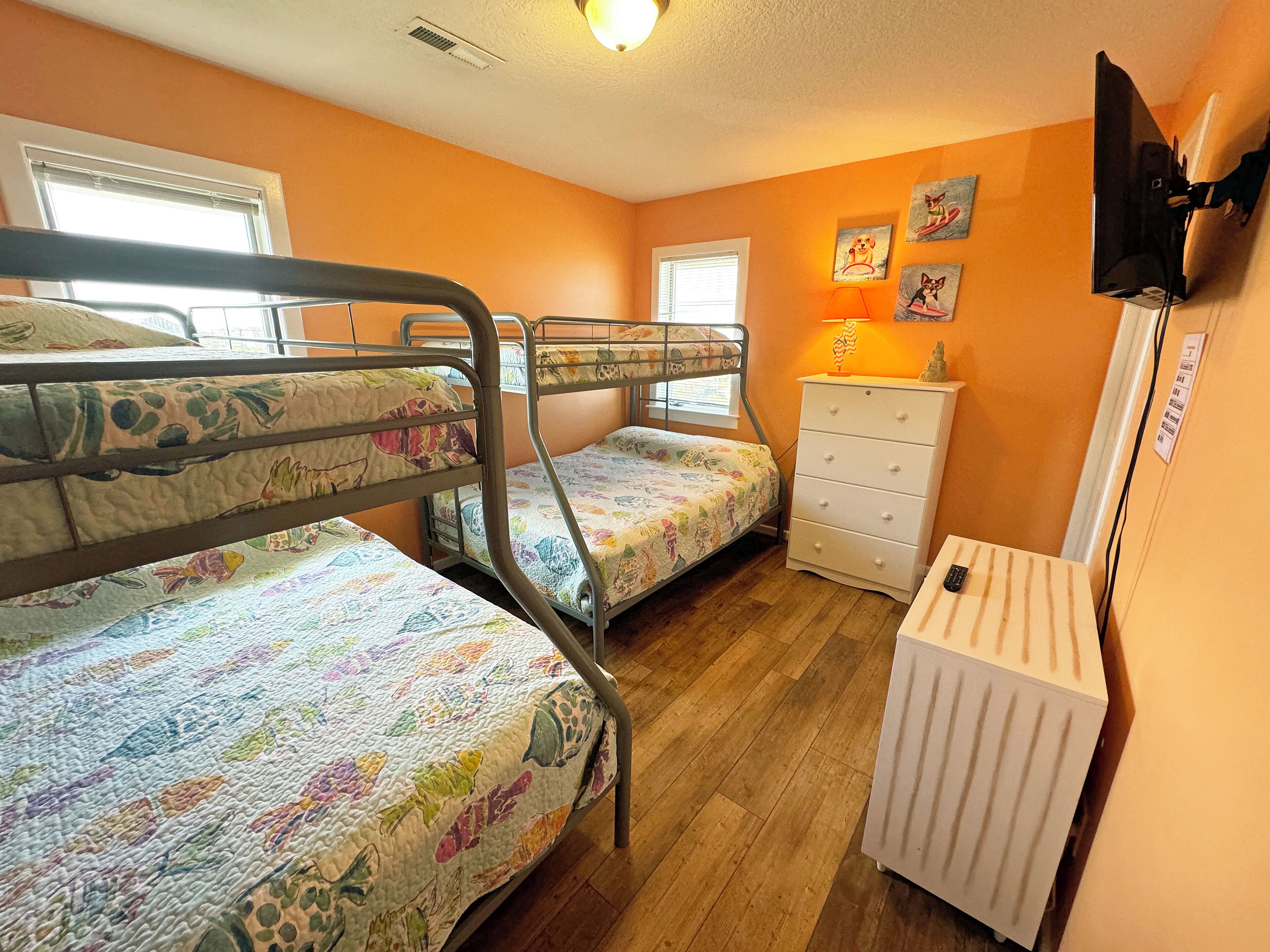Een slaapkamer met twee stapelbedden, een witte dressoir, een radiator en een aan de muur bevestigde televisie.