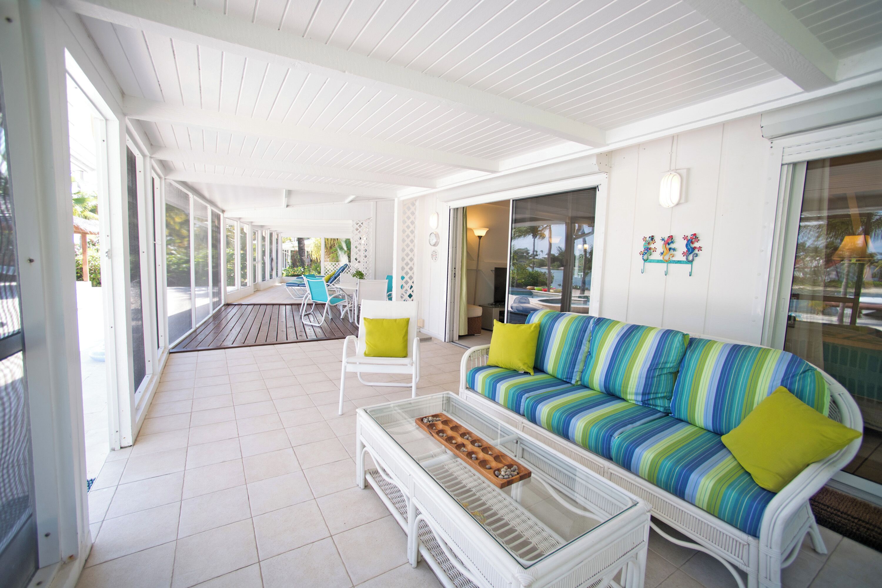 Un patio abrité avec un canapé à rayures, une table basse en verre et une chaise blanche.