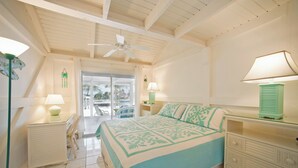Un dormitorio con cama, dos mesitas de noche con lámparas, un ventilador de techo y vistas al exterior a través de un ventanal.