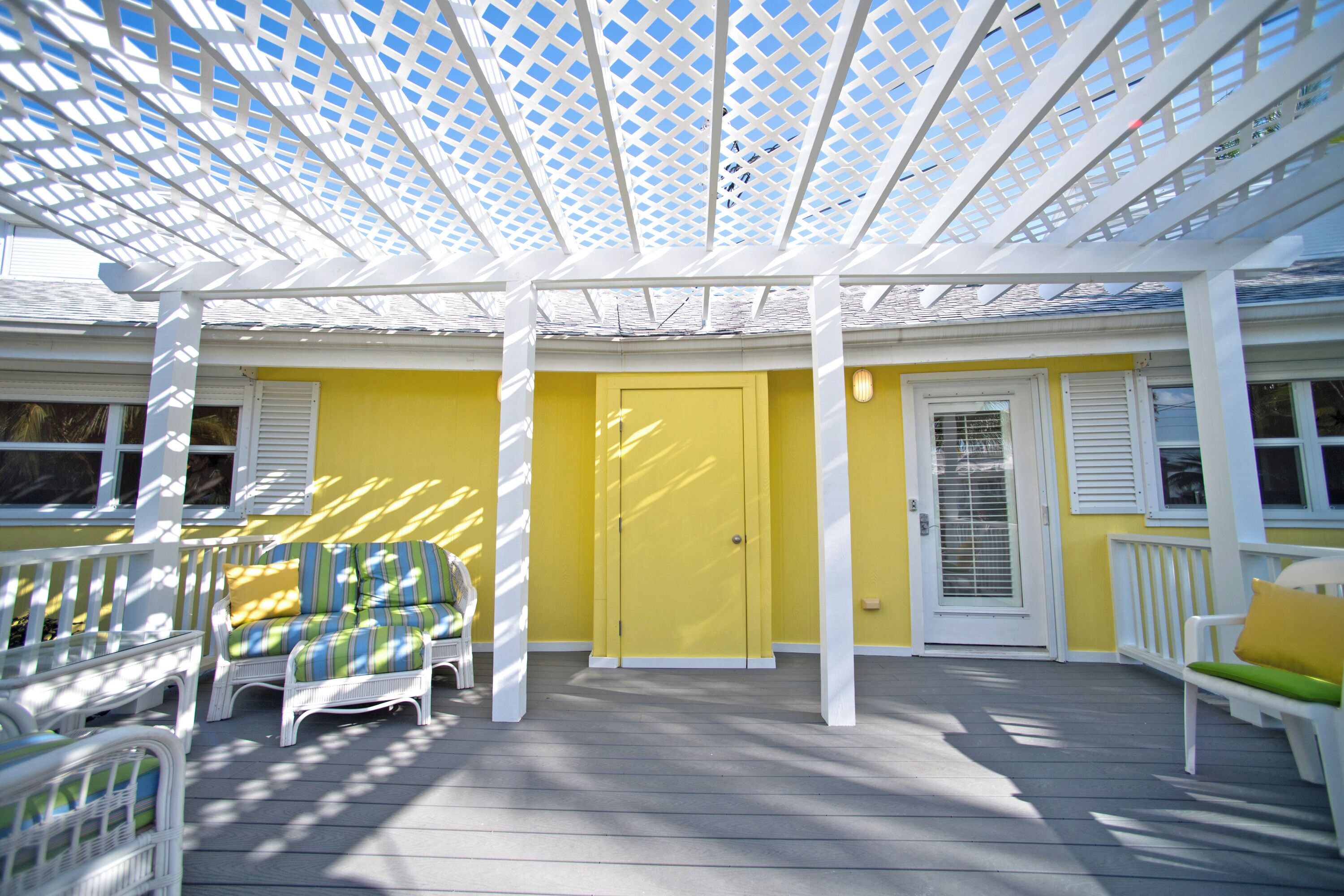 A covered porch with white lattice columns, yellow walls, and white railings.