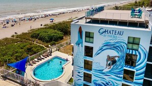 Un hotel con piscina, vista a la playa y un mural de un surfista.