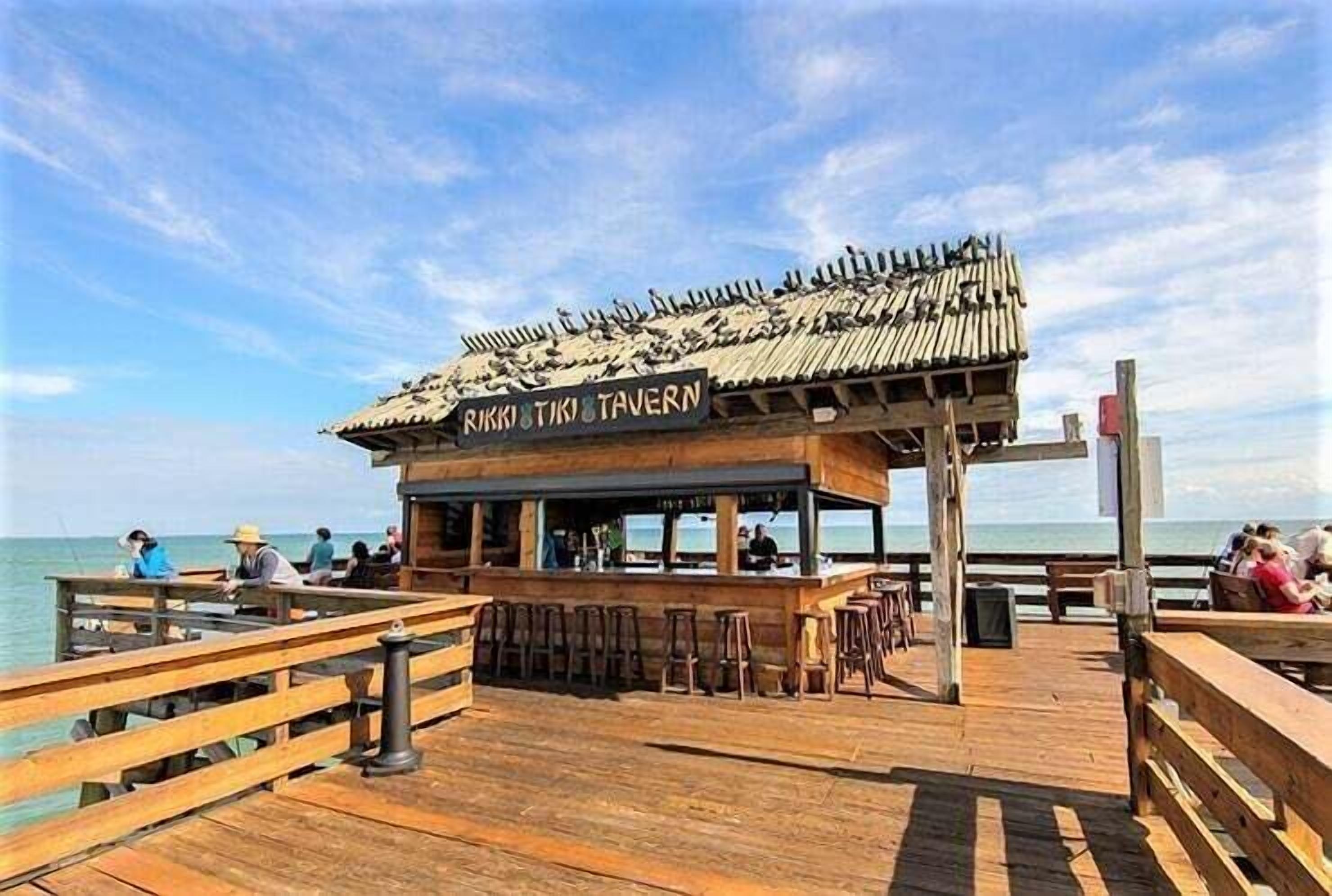 Un muelle de madera con una zona de bar rústica llamada "Rikki Tikki Tavern", con taburetes de madera y una barra.