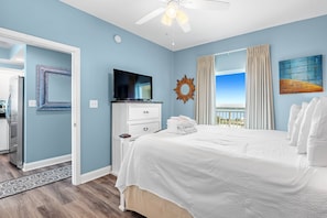 Relax in comfort with a large bed, flat-screen TV, and ceiling fan, surrounded by a peaceful view of the outdoors.