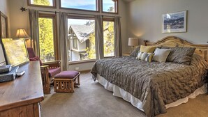 Un dormitorio con una cama grande, dos lámparas de noche, una mesita de noche de madera, un escritorio con lámpara, una silla y una ventana con cortinas.