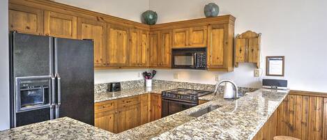 A kitchen with granite countertops, wooden cabinets, a built-in oven, a microwave, and a sink.