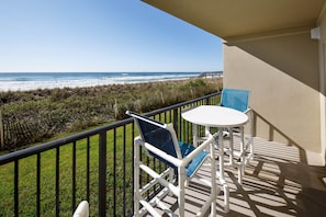 A balcony with a view of the beach, a white table, and a blue chair.