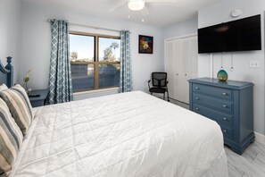 A bedroom with a bed, a dresser, a chair, a TV, and a window with curtains.