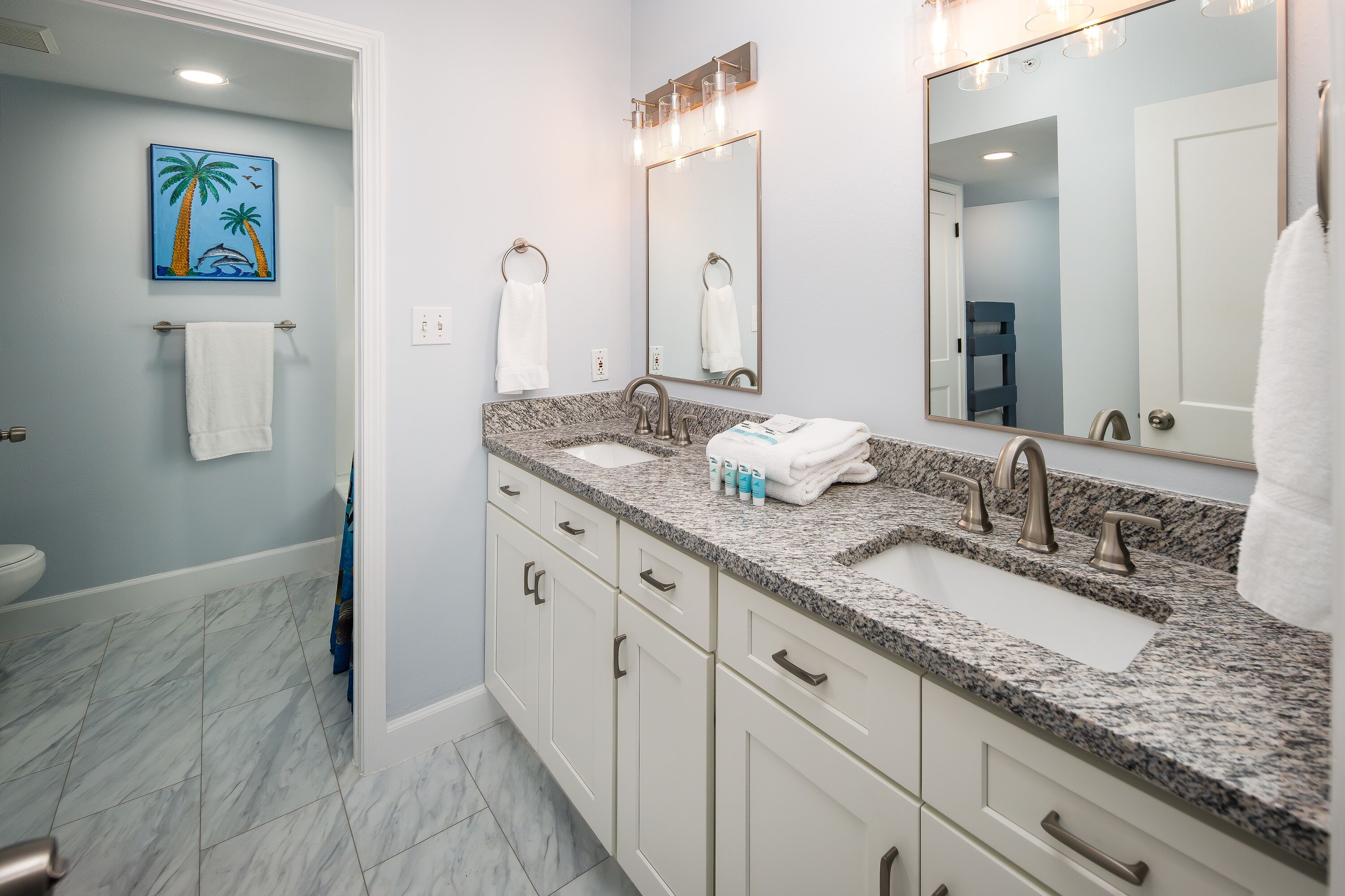 A bathroom with two sinks, a large mirror, and a painting of palm trees.