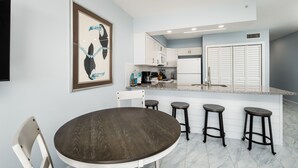 A modern kitchen with white cabinets, a granite countertop, and a round dining table with bar stools. - ETW 1003: Sandy Toes - Where summer is a state of mind! (Fort Walton Beach)