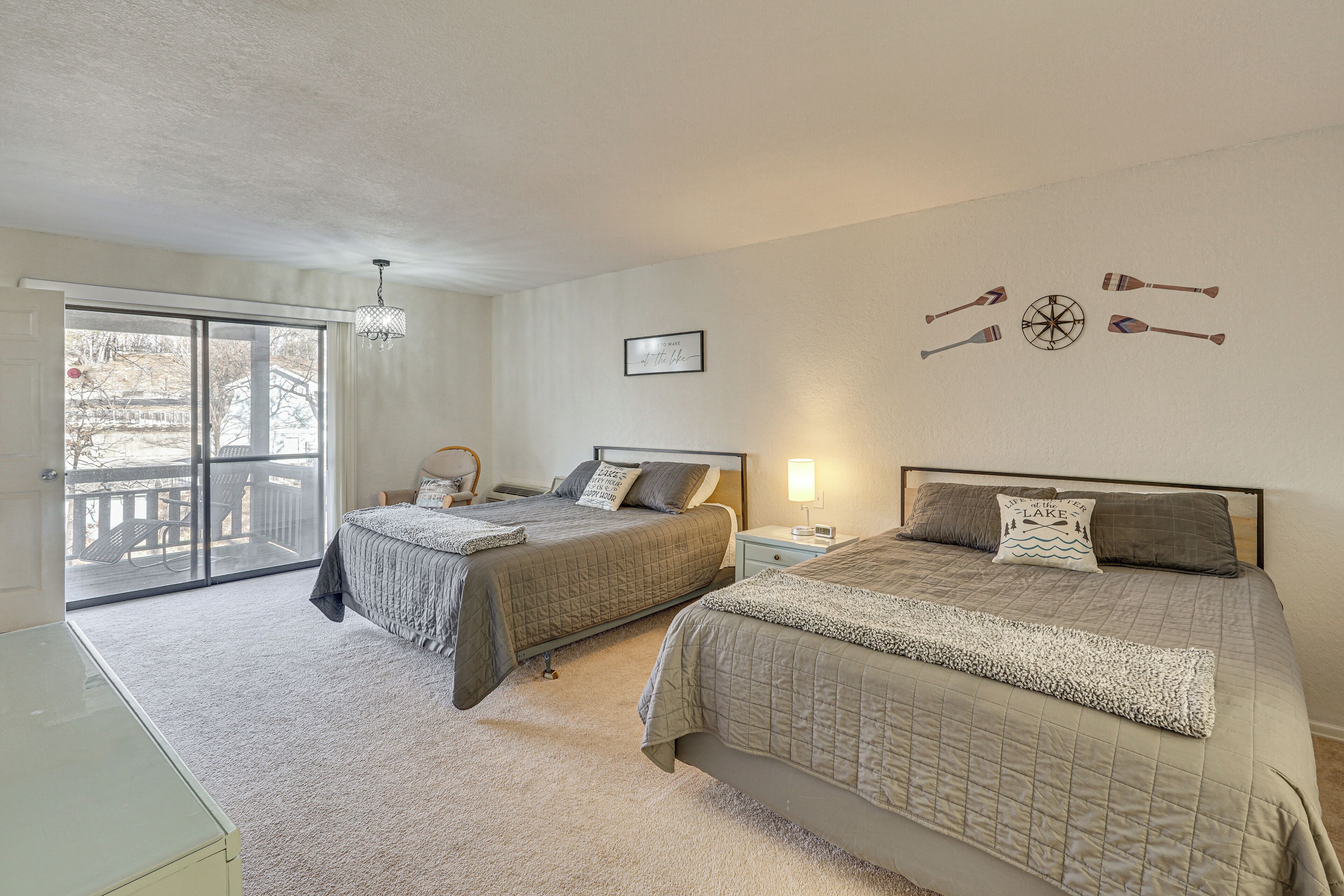 A bedroom with two beds, a large window with a view of a deck, and a ceiling fan.