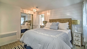 A bedroom with a large bed, a wooden headboard, a mirror, a bedside table with a lamp, and a window with curtains. - Cozy Ocean Grove Beach Retreat: Walk to the Coast! (Ocean Grove)