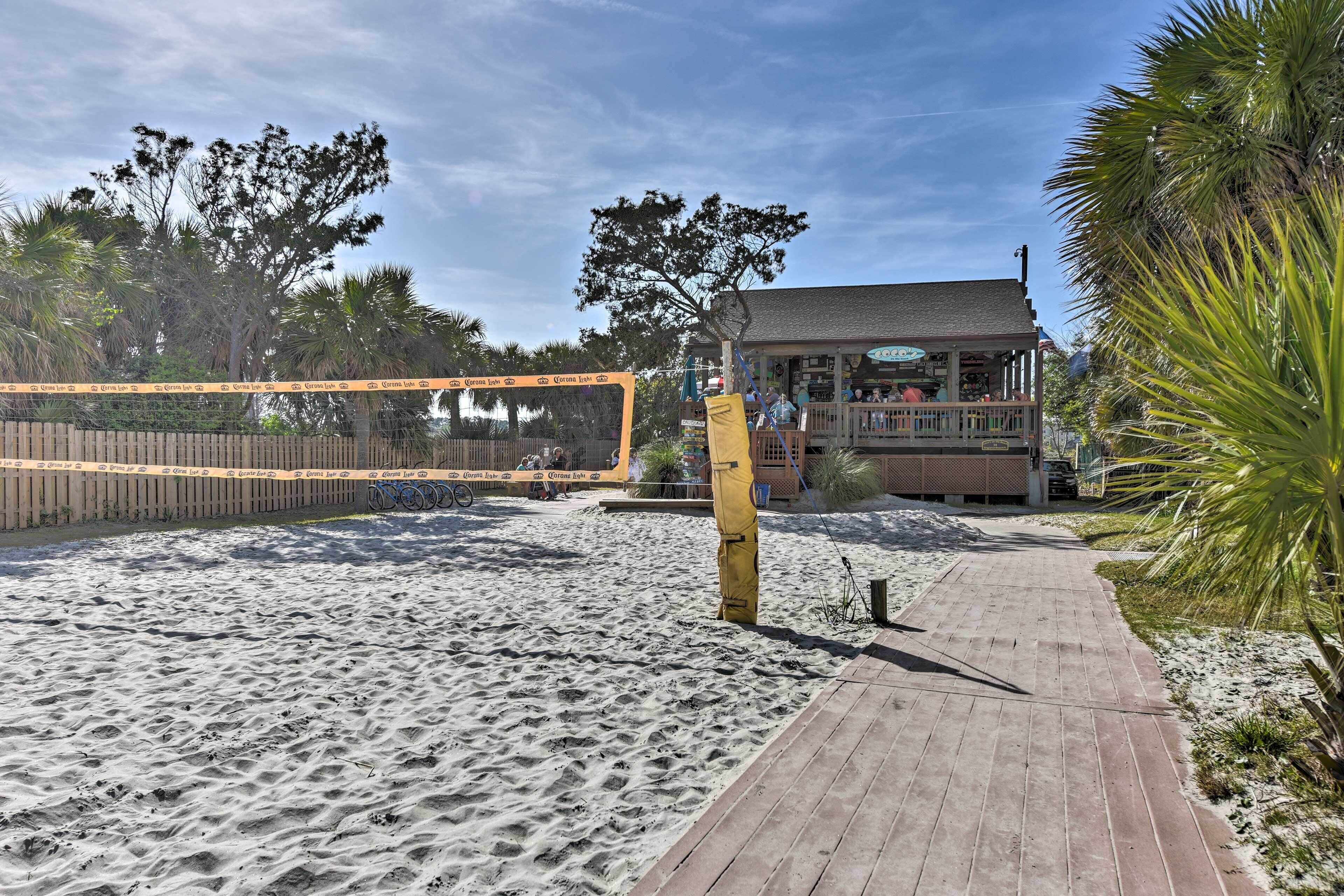Una cancha de voleibol de playa con una pasarela de madera que conduce a un edificio con balcón.