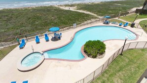 A swimming pool with a hot tub, surrounded by lounge chairs and umbrellas, overlooking a beach.