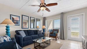 A living room with a ceiling fan, a sofa, a coffee table, and a view of the outdoors through large windows.
