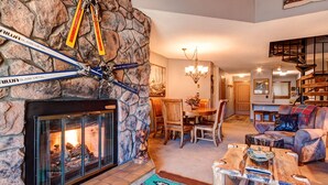 Ein Kamin aus Stein mit Skiern und einem Metallschild, ein Essbereich mit Stühlen, ein Kamin, eine Chandelüster, ein Sofa und eine Treppe.
