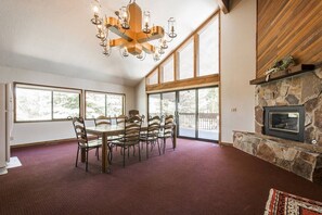A dining area with a large table and chairs, a stone fireplace, and large windows.