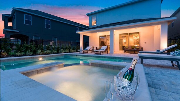 Une maison moderne avec une piscine, des chaises longues et une bouteille de champagne.