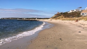 Una playa con arena, un rompeolas rocoso y una hilera de casas en una colina.