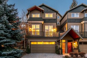A two-story residential building with a garage, a balcony, and a red door.