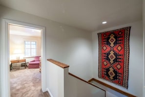 A hallway with a carpeted floor, a wooden handrail, and a patterned wall hanging.
