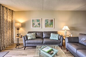 A living room with a dark brown leather sofa, a glass coffee table, and two wall-mounted lamps.