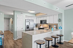 Une cuisine moderne avec des meubles blancs, un îlot central doté de tabourets, un four à micro-ondes et un réfrigérateur.
