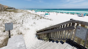Ein Strand mit einer Holztreppe, die zum Sand führt, einem Hinweisschild und einem Verbotsschild gegen Littering.