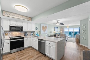 Une cuisine moderne avec des meubles blancs, un four à micro-ondes et un lave-vaisselle. Un coin repas offre une vue sur la mer.
