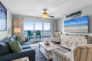 A living room with a sofa, armchair, coffee table, TV, and a balcony with chairs.