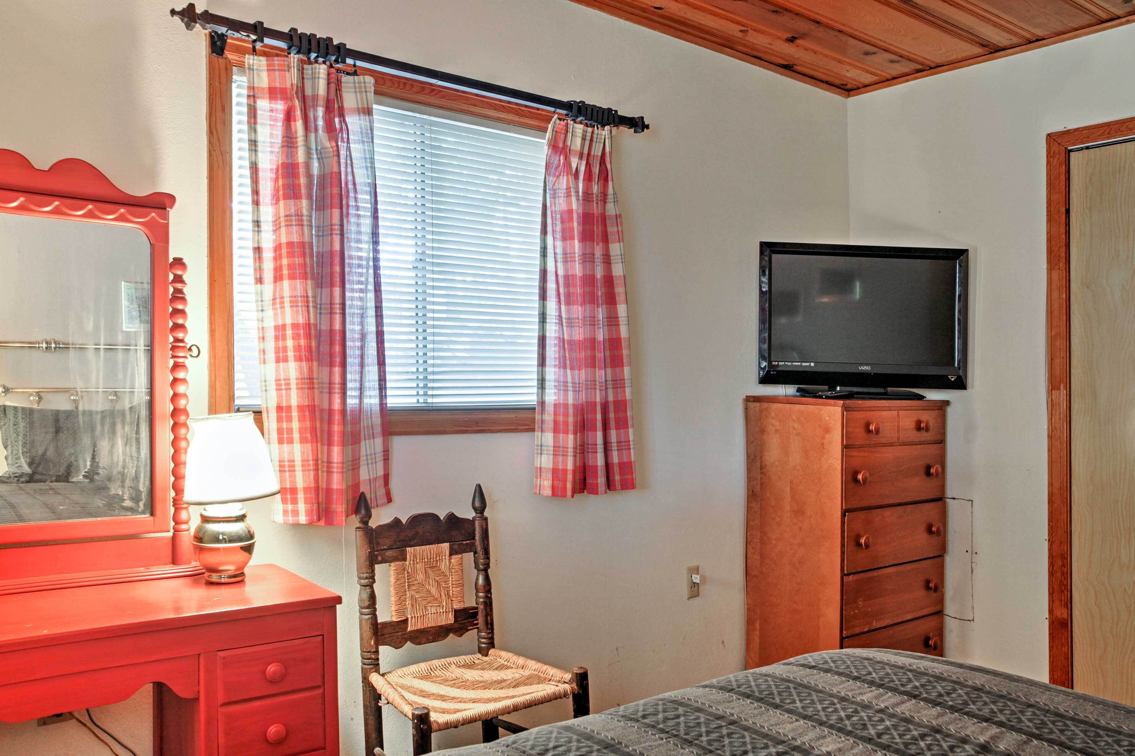 A bedroom with a bed, a dresser, a chair, a television, and a window with curtains.
