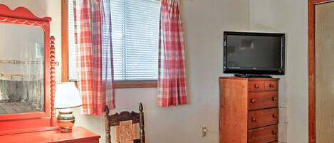 A bedroom with a bed, a dresser, a chair, a television, and a window with curtains.