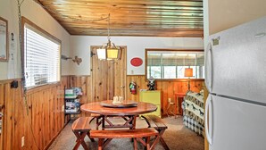 A wooden-paneled kitchen with a round wooden table and benches, a refrigerator, and a hanging light fixture. - Ruidoso Log Cabin Near Skiing & Wildlife! (Ruidoso)