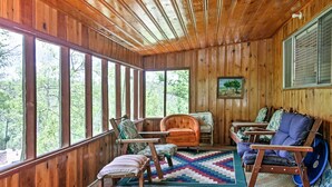 A wooden cabin interior with large windows, a cozy seating area with chairs and a couch, and a quilted rug on the floor. - Ruidoso Log Cabin Near Skiing & Wildlife! (Ruidoso)