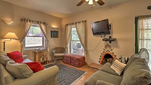 Ein gemütliches Wohnzimmer mit einer Couch, Sesseln, einem Fernseher, einem Kamin und einem Deckenventilator.
