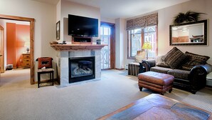 A living room with a fireplace, a television mounted above it, a sofa, and a coffee table. - Walking distance to Main Street. Pool and Hot Tubs with a Beautiful View! (Breckenridge)
