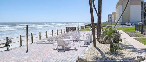 A seaside patio with outdoor seating, palm trees, and a view of the ocean.