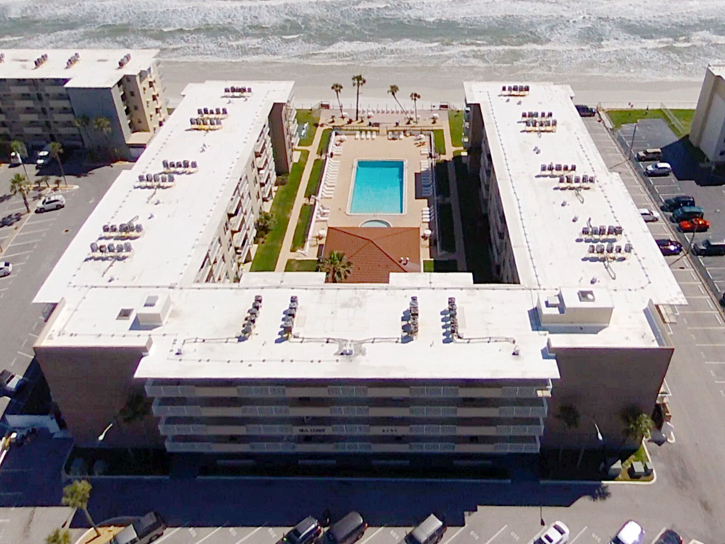 Een groot hotel met een centraal gelegen zwembad, meerdere parkeerlagen en uitzicht op het strand.