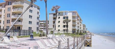 Un hotel frente a la playa con varios balcones, palmeras y una playa de arena.