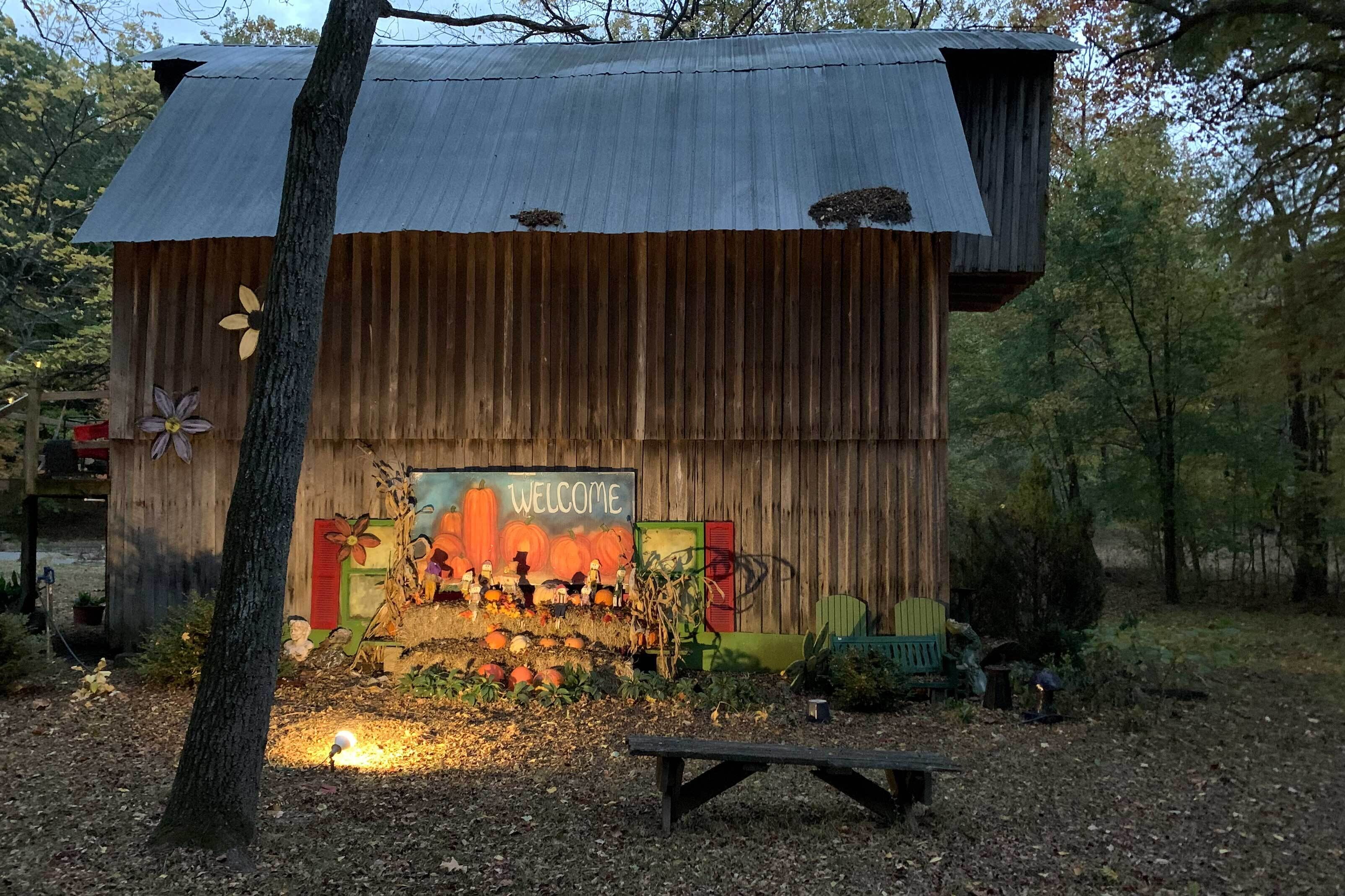 A rustic wooden structure with a 'WELCOME' sign, surrounded by autumn foliage and pumpkins.