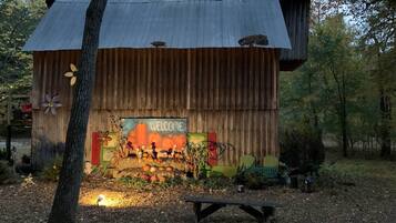 A rustic wooden structure with a 'WELCOME' sign, surrounded by autumn foliage and pumpkins.