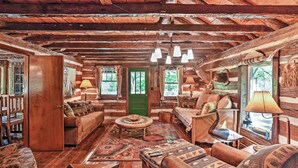 L’intérieur d’un chalet rustique, avec des poutres en bois, une porte verte et un coin salon accueillant agrémenté de coussins à motifs et d’une table basse ronde.
